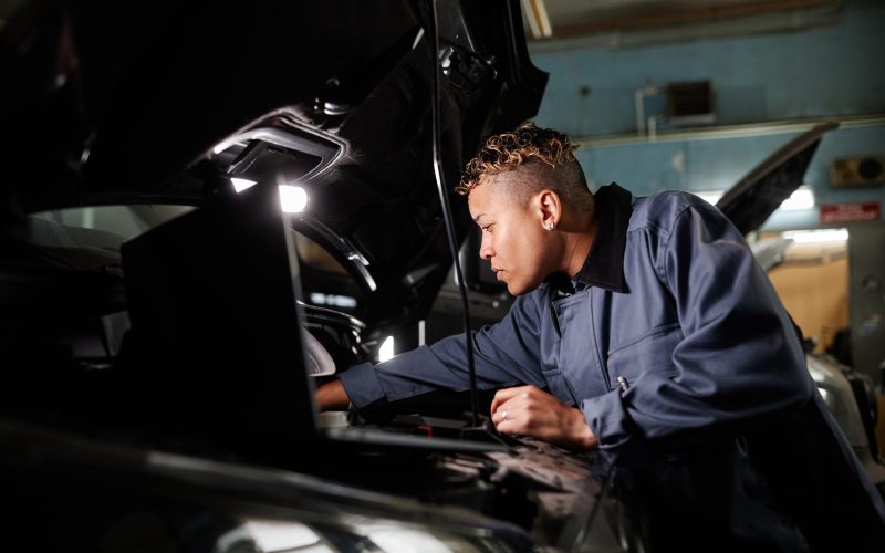 Side view portrait of female mechanic repairing truck engine in garage with accent light